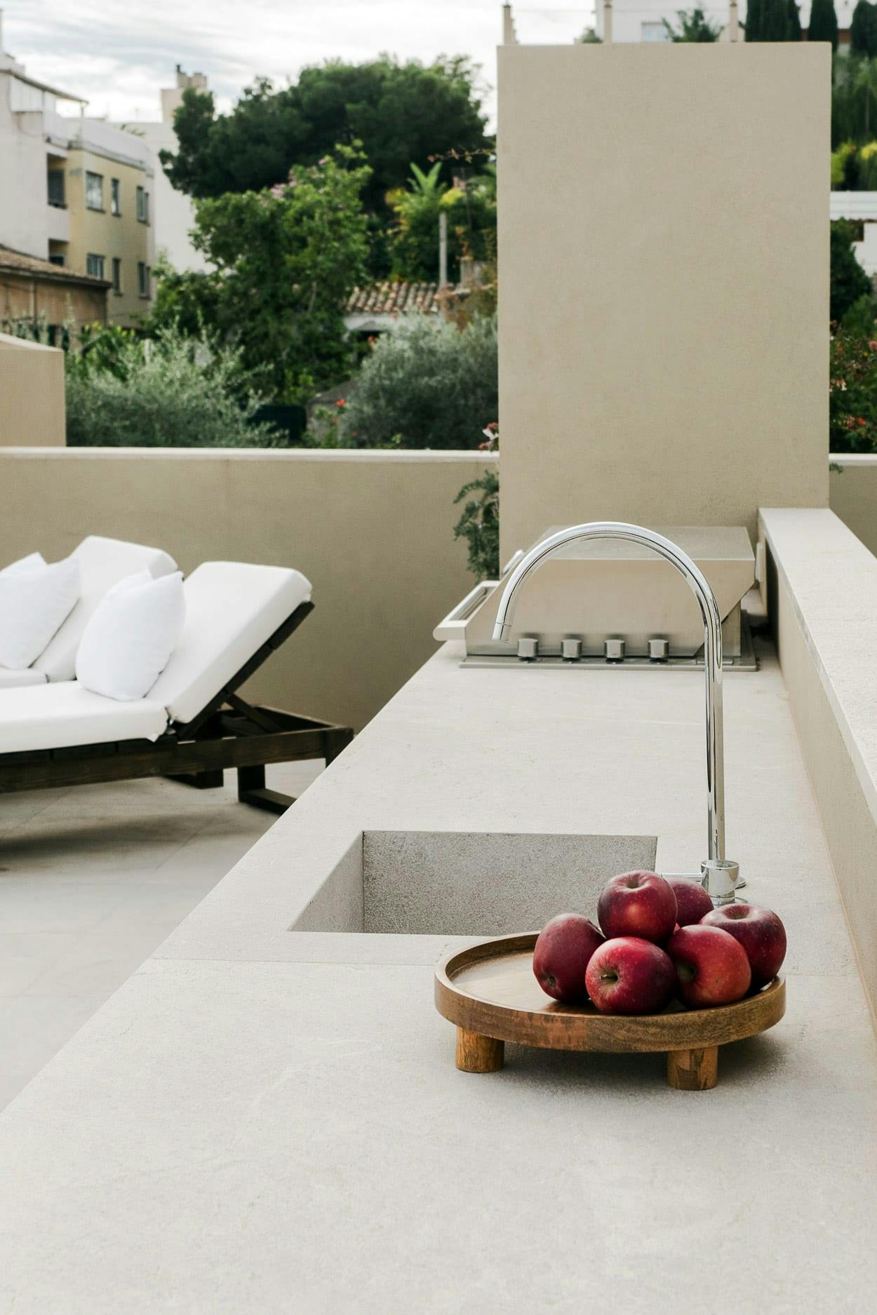 The image features a white bathroom with a sink, a bathtub, and a large bathtub filled with water. There is a wooden bowl on the countertop with a variety of fruits, including apples and oranges, placed on it.