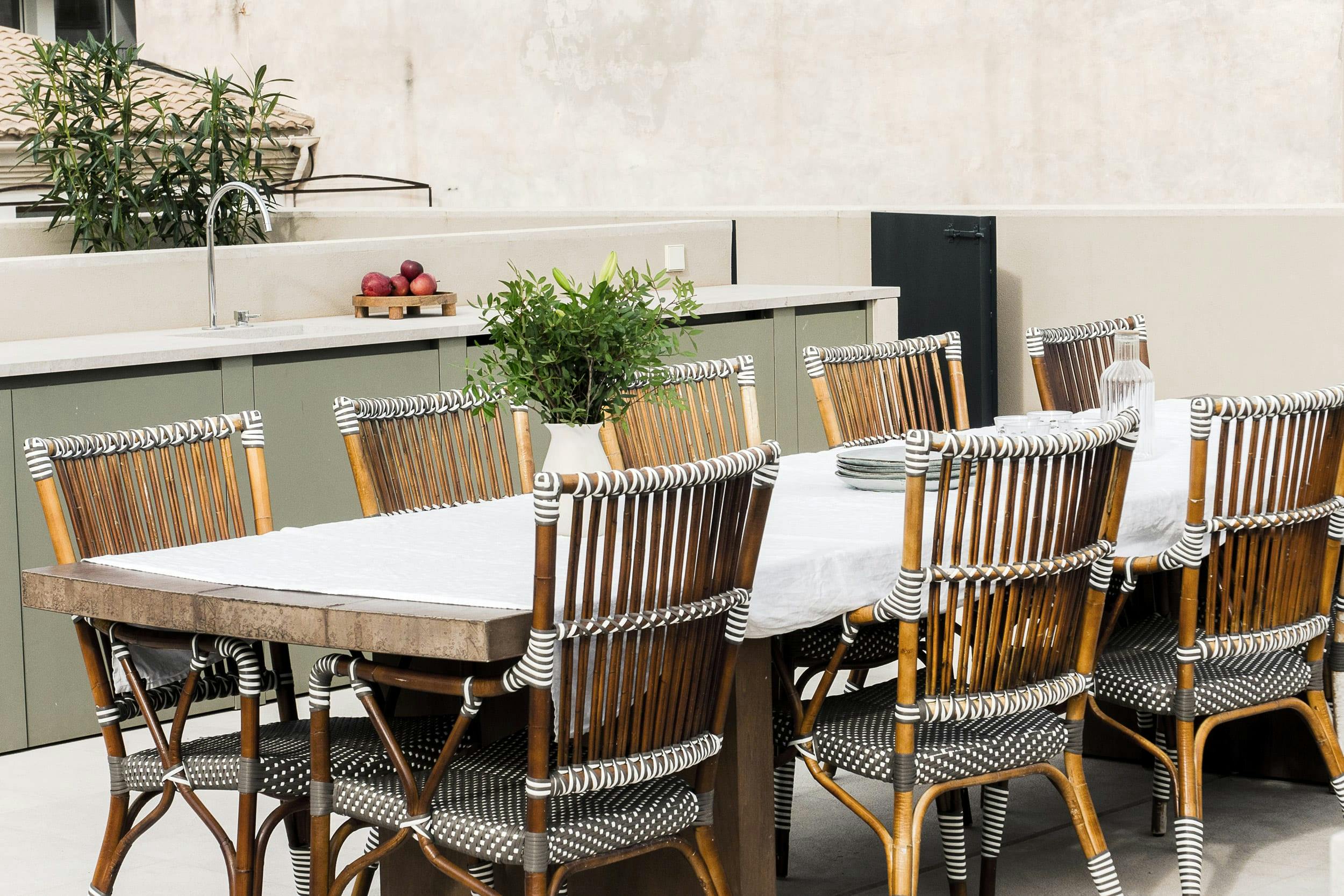 The image features a large outdoor dining area with a table and chairs, surrounded by a patio with a potted plant and a vase.