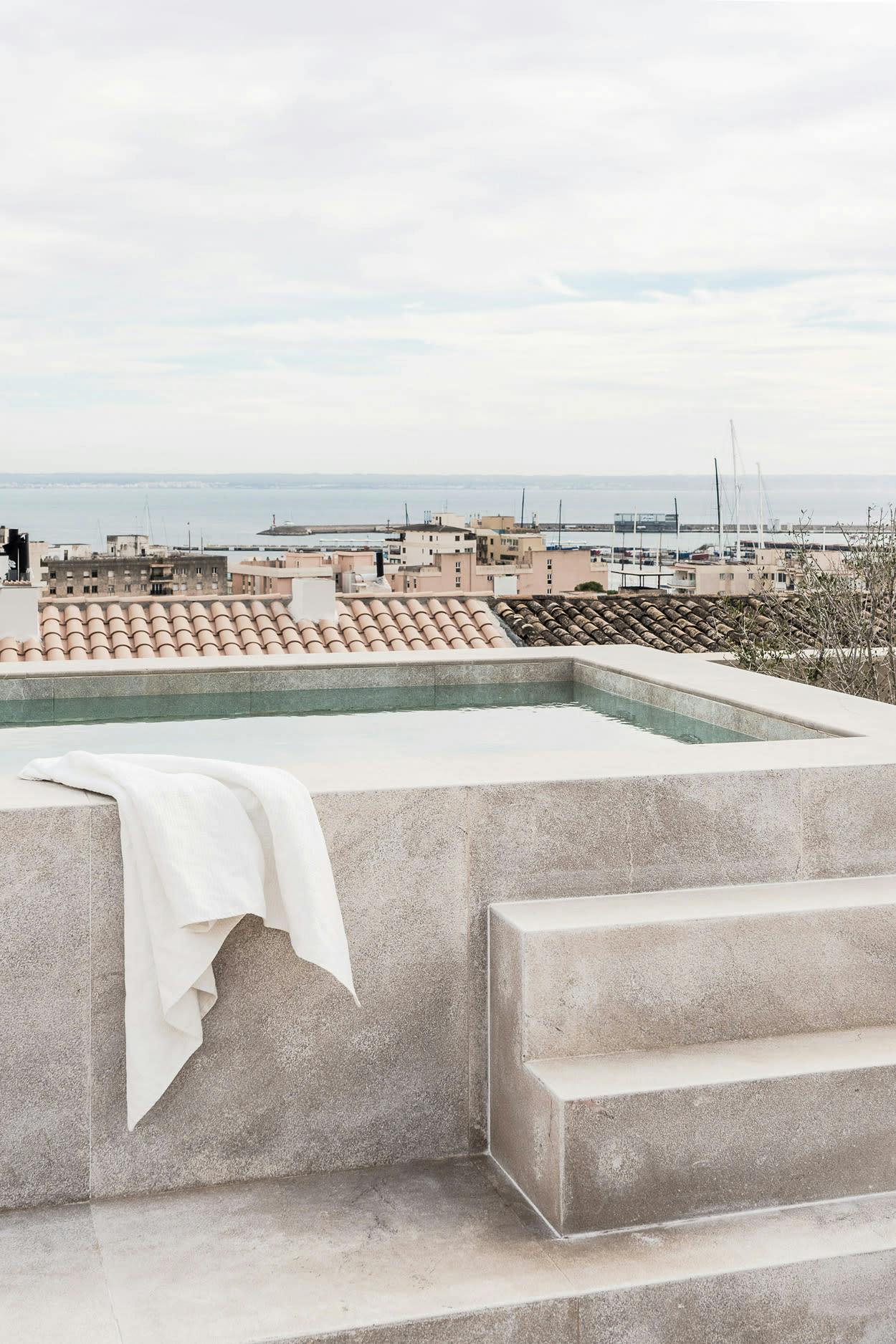 A large concrete pool with a white towel is located on a rooftop overlooking the ocean.