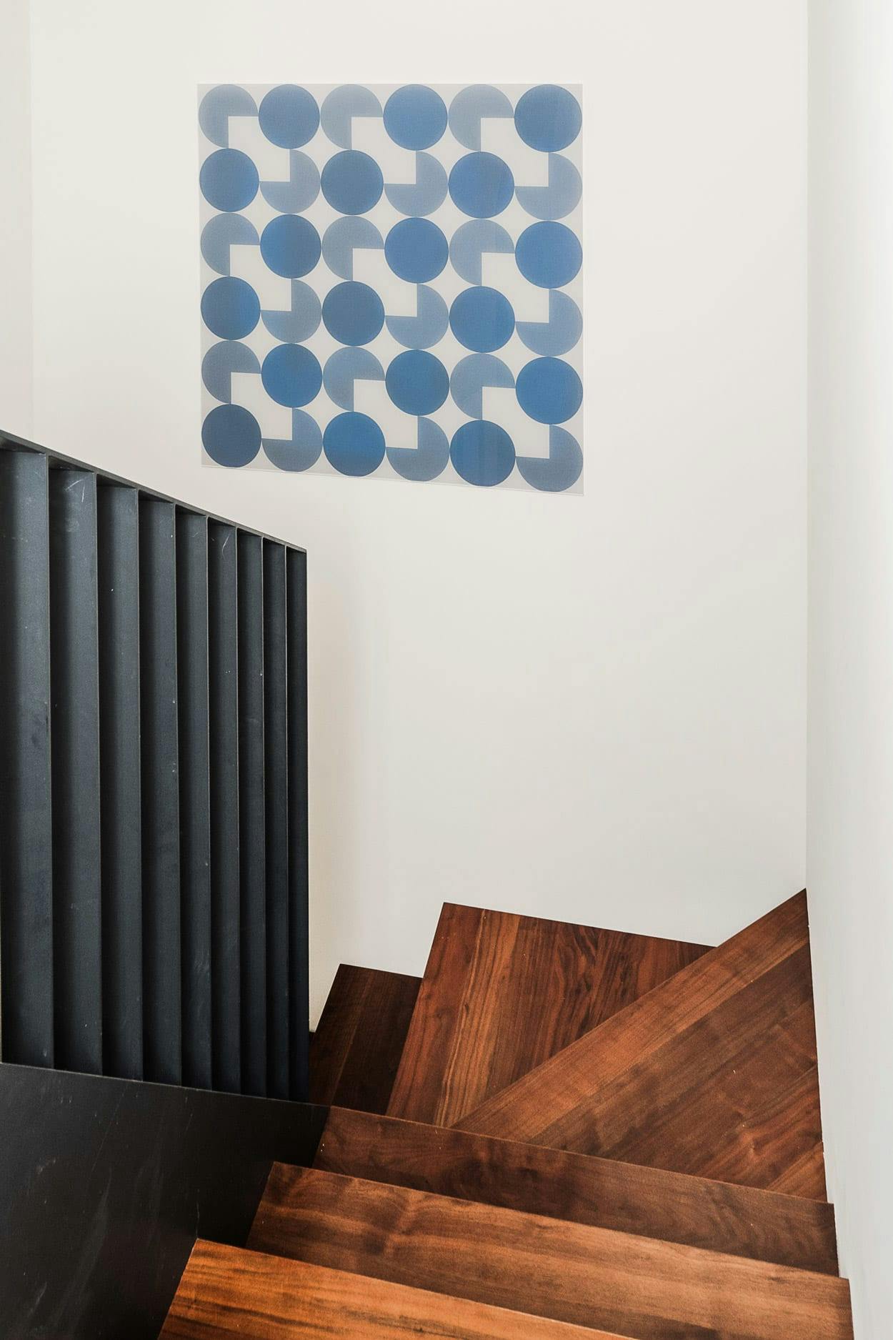 A large wooden staircase with a black railing is situated next to a wall with a blue and white patterned wallpaper.